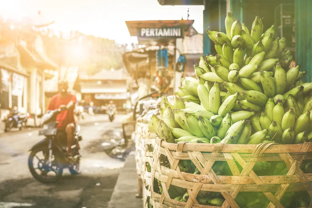 Woven baskets stacked with green fruit beside a street in a Southeast Asian town